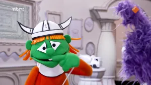Een foto van een groene pop met een Viking helm op die met de wijsvinger onder de neus zit. Ernaast staat een paarse pop te kijken.