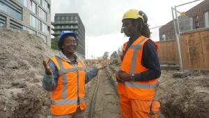 Een foto van presentator Tirsa die met een kabelwerker staat in een tijdelijke put waar kabels worden aangelegd.