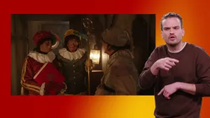 Een foto van drie pieten die met elkaar praten. Eentje heeft een Sinterklaas boek in handen, en een ander houdt een Sinterklaas staf vast. Op de voorgrond wordt het vertolkt door een tolk.