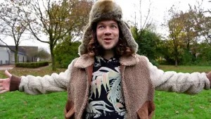 Foto van presentator Pascal die buiten staat op een grasveld en een winterjas en Russische bontmuts draagt.
