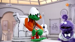 Foto van groene pop die zit op een witte stoel en kijkt naar de presentator, een paarse pop.