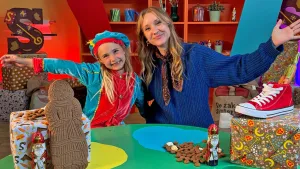 Presentator Rosalie en kind met hand in de lucht in kamer vol met cadeautjes en snoepgoed.