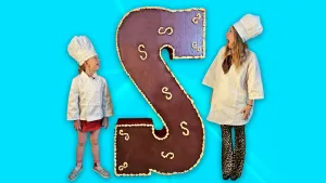 Foto van levensgrote versierde chocoladeletter. Er staat een kind en presentator Rosalie naast.aast