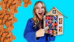 Foto van presentator Rosalie die wijst naar versierde adventkalender in de vorm van een huis die ze vasthoudt.