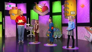 Een foto van presentator Daan die samen met drie kinderen het Raad Eens Wat Ik Doe spel speelt in de studio.