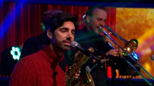 Foto van zanger Ruben Hein achter microfoon met blazers op de achtergrond in studiosetting.