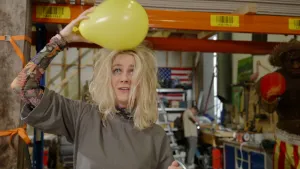 Foto van presentatrie Janouk die gele ballon over haar haar wrijft waardoor het overeind gaat staan.