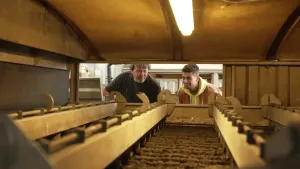 Op deze afbeelding kijkt de presentator samen met de expert naar de machine waarin de drab van het rioolwater in wordt verwerkt. Het perspectief is vanuit de machine en de drab ziet eruit als poep.