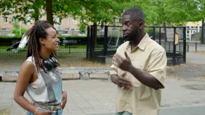 Foto van presentator Eva in gesprek met een rapper op een buitenspeelplein.