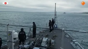 Foto van het dek van een marineschip op zee met bemanning die over het water uitkijkt.