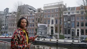 Presentatrice Astrid staat aan de gracht. Ze houdt een foto vast van een grachtenpand
