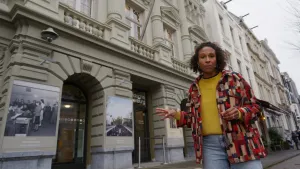 Presentatrice Astrid staat voor een wit gebouw met bogen.