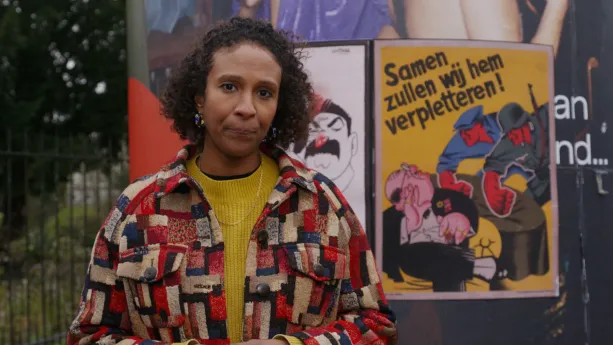 Astrid staat naast een zuil. Hierop hangen propaganda posters