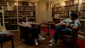 Foto van jong meisje en donkere jongen met dreads in antiek ogende bibliotheek.