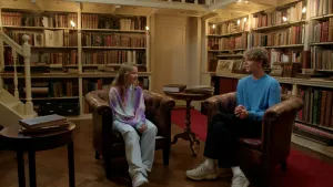 Foto van 10-jarig meisje en 20-jarige jongen in een antiek ogende bibliotheek, met boekenkasten op de achtergrond.