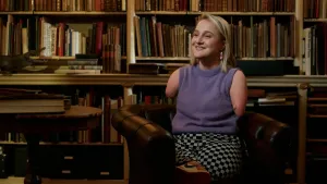 Foto van blonde lachende vrouw zonder armen en benen op stoel in bibliotheek.