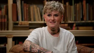 Foto van jonge vrouw met kort blond haar en tatoeages op haar arm en in haar nek.