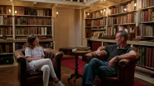 Foto van 13-jarig meisje en man van middelbare leeftijd op bruine leren stoelen in antieke bibliotheek.