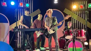 Foto van acteurs die de band Doe Maar naspelen, met gitaren, keyboard en drumstel op een podium.