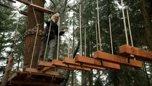 Foto van presentatrice Janouk Kelderman die een houten parcours in een klimbos aflegt.