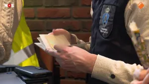Foto van een man met een vestje met logo van Koninklijke Marechaussee die door een paspoort bladert.