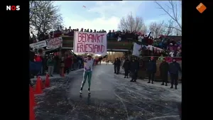 Foto van schaatser die een spandoek hoog houdt met erop 'Bedankt Friesland'. Aan de randen van het ijs en op de brug juichen veel mensen.
