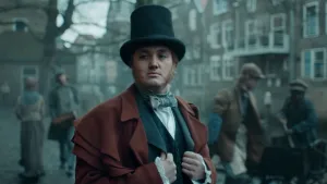 Foto van deftig uitziende man in rode jas en met zwarte hoed in een straat ergens in de 19e eeuw