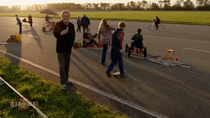 Foto van snelweg waarop kinderen aan het spelen zijn in de schemering, een presentator met een microfoon in zijn hand kijkt in de camera.