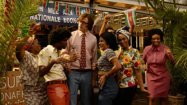 Foto van verslaggever tussen Surinaamse mensen tijdens viering van de onafhankelijkheid van Suriname in 1975, geensceneerd.