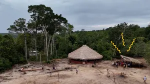 Foto van dorpje in jungle met een plaggenhut en een schuurtje waar zonnepanelen op liggen.