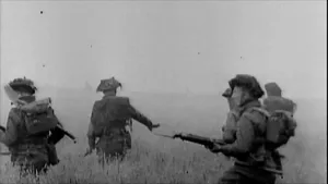 Zwart wit beeld van een aantal soldaten die gewapend door een veld lopen.