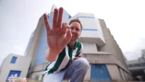 Een foto van de presentator. Hij zit buiten, geknield voor een kantoorgebouw, en toont een microchip aan de camera. Hij heeft het tussen zijn duim en wijsvinger vast. Het is amper een centimeter groot.