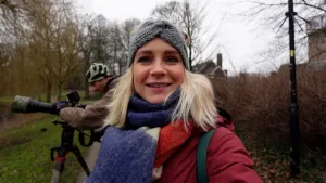 Foto van presentatrice Janouk met p de achtergrond een man met een camera met telelens op een statief.