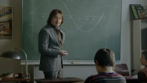 Foto van ouderwets geklede docent voor een schoolbord in de klas met in zijn hand een brandende sigaret.