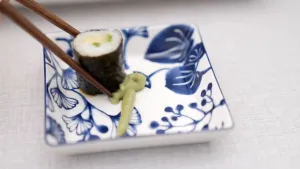 Foto van stukje sushi dat met stokjes in wasabi wordt gedoopt.