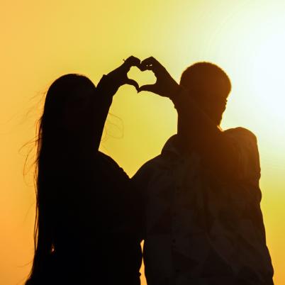 Een foto van een man en een vrouw die tijdens zonsondergang samen met hun handen een hartje vormen