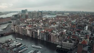Een foto van Amsterdam in het heden, met een gracht en grachtenpanden, de foto is van boven genomen op een grijze dag.