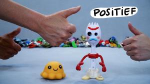 Een foto van drie verschillende opgestoken duimen met daarbij het woord "positief" en daaronder twee speelgoedpoppetjes waarvan de ene glimlacht en de andere fronst