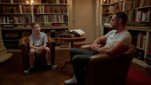 Foto van jongen in gesprek met gespierde man in oude bibliotheek.