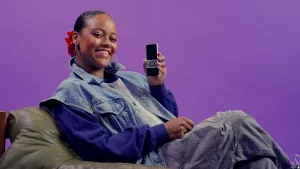 Een foto van presentatrice Quinty op een zitzak, ze houdt een telefoon in haar hand omhoog, de achtergrond is paars.