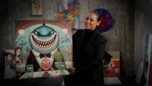 Een foto van presentatrice Quinty die een kunstwerk omhoog houdt wat door AI gegenereerd is, er staat een haai op in cartoonstijl.