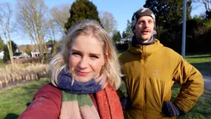 Een selfie van Janouk en Bram, ze staan in een voortuin in de zon, zij heeft een kleurige sjaal om, hij heeft een muts op.