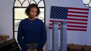 Presentatrice Astrid staat voor een raam. Rechts van haar staan de Twin Towers en erboven een Amerikaanse vlag.