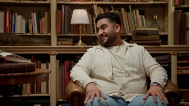 Foto van volkszanger Ammar lachend in een oude bibliotheek.