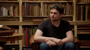 Foto van jongen met donker haar en baardje in oude bibliotheek.