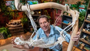 Freek Vonk die poseert achter het skelet van een luiaard die aan een dikke tak hangt.