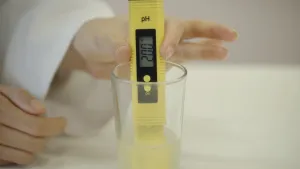 Een hand houdt een geel staafje vast en dompelt deze onder in een glas.