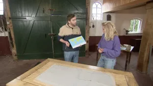 Twee mensen staan achter een tafel met zand erop. De man houdt een wereldkaart vast.