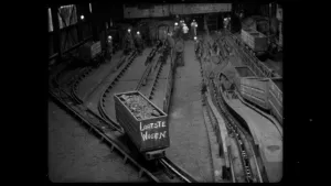 Een zwart-wit foto van een mijnkarretje met de tekst Laatste weken, het karretje staat op rails.