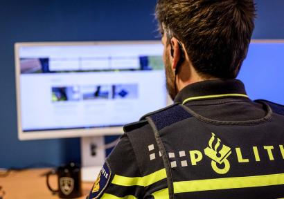 Foto van politieagent in uniform achter computerscherm, van achteren gezien.